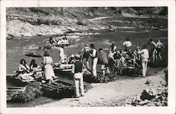 Men and women enter rowboats on a riverbank Postcard