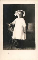 Little Girl in White Dress next to a Crib Postcard