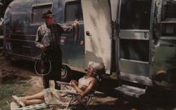 Man showing fish to woman by trailer Postcard