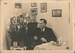 Man Seated at Table with Christmas Tree Postcard