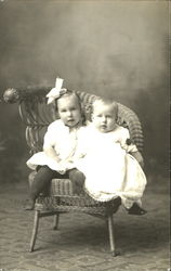 Two Young Children sitting in a Wicker Chair Postcard