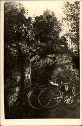 People standing on a rock ledge looking down at bikes Postcard