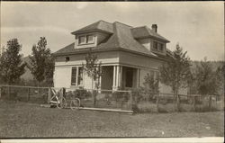 Clapboard house, with bicycle leaning on fence Postcard