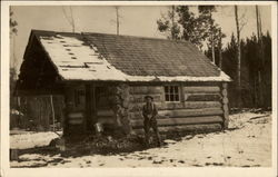 Man with gun outside log cabin Buildings Postcard Postcard