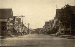 View Down Residential Street with American Flags Hanging from Houses Postcard