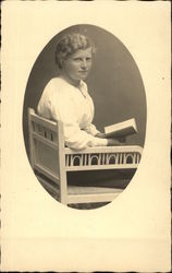 Woman in chair holding open book Postcard