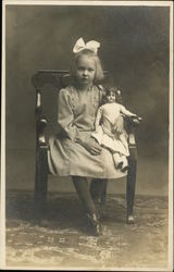 Little Girl with White Bow in Hair Holding Doll While Sitting in Chair Children Postcard Postcard