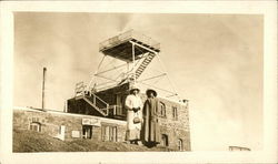 Two Women Posing In Front of Large Brick Building Postcard