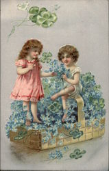 Young boy and girl sitting in a basket of flowers. Postcard