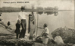 Man holding a giant fish with two children looking Bemidji, MN Postcard Postcard Postcard