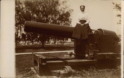 Woman Perched Atop Large Cannon in Park Setting Postcard