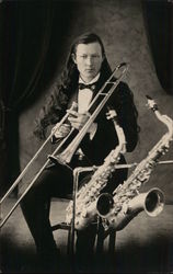 Long-Haired Man Holding Trombone, Two Saxophones Nearby Postcard