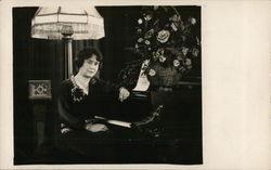 Woman sitting in front of piano. Postcard