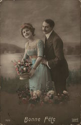 A moustached man stands behind a woman in a blue dress holding a flower arrangement with the caption "Bonne fête" below Postcard