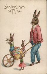 Easter Joys be Thine. Dad rabbit wearing a suit pushes a wheelbarrow of eggs. Three bunnies accompany. With Bunnies Postcard Pos Postcard