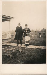 Family Standing Outside Home, Old Toy Wagon Postcard