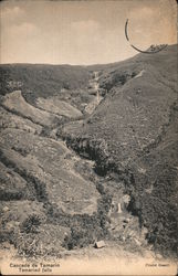 A waterfall descending from a rocky and tree lined plateau Postcard