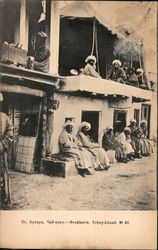 Men sitting and smoking along a two story building Postcard