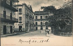 A street with three story buildings and a park with pedestrians Postcard