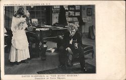 A man sitting on a piano bench reading a pamplet and a woman standing beside the piano. Postcard