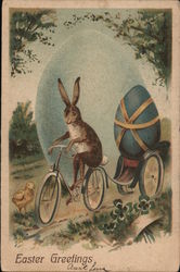 Easter Greetings - Bunny riding a bike pulling an egg on a wagon with a chick watching Postcard