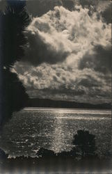 Sun or Moon reflecting on water with mountains, clouds, and trees Postcard