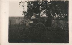 Toddler sitting in open buggy, no horse, picket fence Children Postcard Postcard Postcard