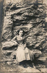 Girl with watch pin on dress sitting on natural cliff seat. Postcard