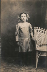 Portrait of young girl standing beside a chair Postcard