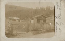 Wooden Homes Behind a Wooden Picket Fence and Gate Postcard