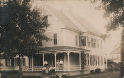 Historical photo of 8 adults and one young child in front of large Victorian house. Postcard