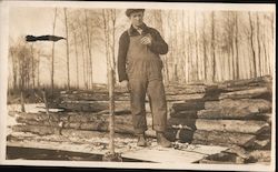 Man in Insulated Overalls in Front of Log Pile Postcard