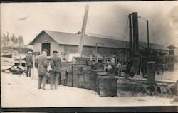 Men standing in a shipyard looking at wooden boxes Postcard