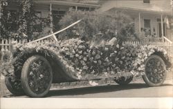 A Man and Woman in a Car That is Covered By Flowers Postcard