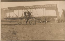 two wing box plane parked in field in front of another Postcard