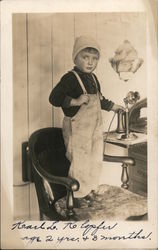 Boy in overalls standing on chair holding telephone Postcard