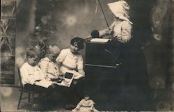 Four children playing school with dolly on floor, teacher with horse whip Postcard