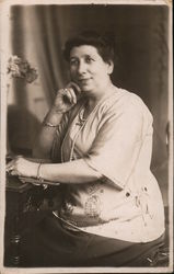 Dark-Haired lady with pearl necklace sitting at desk Postcard