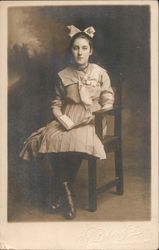 Studio portrait of young girl sitting in chair with a book Postcard