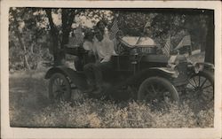 Two couples sitting in car decorated with flags. Postcard