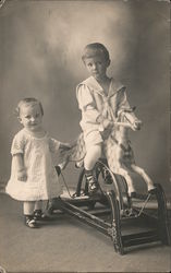 Little boy on a hobby horse with a little girl standing next to him Postcard