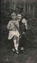 Man, girl, and ventriloquist dummy sitting outside Postcard