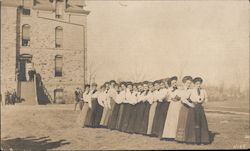 Row of young women in front of school. Postcard