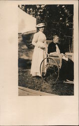 Young woman stands behind wheelchair of older woman Postcard