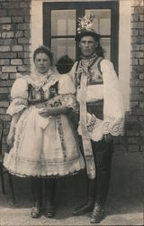 Man and Woman in native costume pose by a brick building Postcard Postcard Postcard