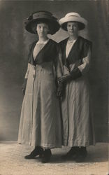 Two ladies wearing similar coats and gloves, and different hats Postcard