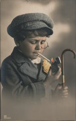 A young boy, with hat, cane and monocle lights a cigarette. Children Postcard Postcard Postcard