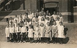 Children posing as a group outside a brick building Postcard