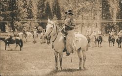 Cowboy on a white horse with more horses with riders in back Postcard