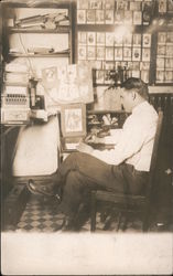 A Man Sitting at a Desk Drawing, Postcards on Wall Postcard